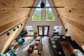 Ein Innenraum mit hohen Decken, Holzausstattung, einer Essecke, Sitzmöglichkeiten und Blick durch ein großes Fenster.