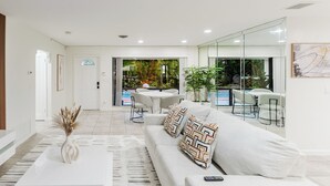 A modern living room with a white sofa, a coffee table, and a dining area with chairs and a table. - Paradise in Pompano: Heated Pool, Dock, Water View (Pompano Beach)
