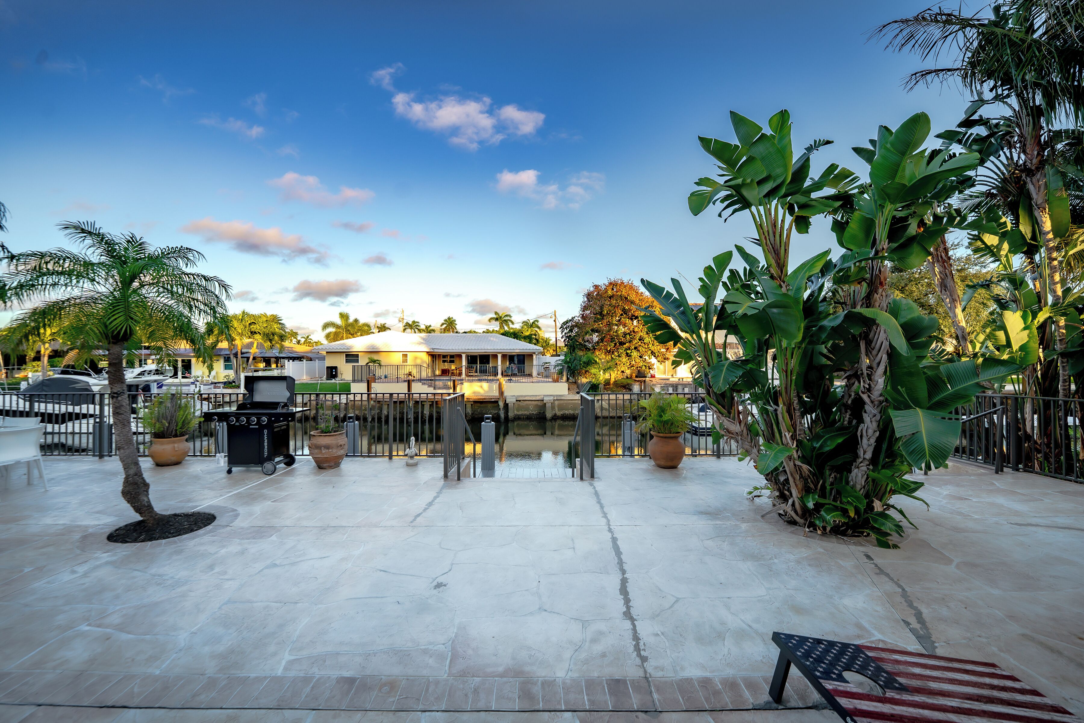 An outdoor patio area with a grill, potted plants, and a view of a building in the background.