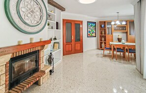 A living room with a fireplace, a dining area with a table and chairs, and a kitchen area with cabinets and a countertop. - Amazing home in Alhaurín de la Torre (Alhaurín de la Torre)