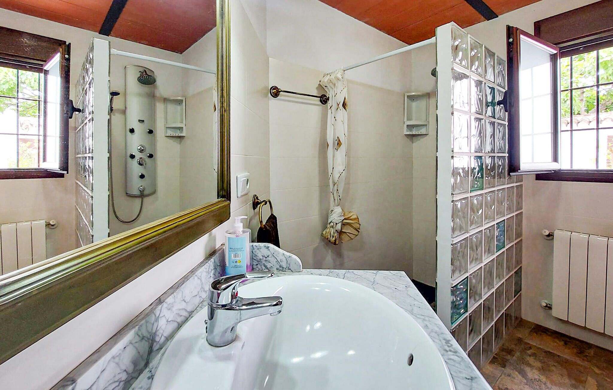 A bathroom with a large mirror, a white sink, a shower, and a glass shower enclosure.
