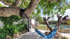 Eine Hängematte unter einem Baum, ein Pool und ein weißes Gebäude mit einem Holzzaun.