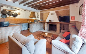 Een moderne woonkamer met een open haard, een keukenhoek met een metselwerk achterwand en een televisie.
