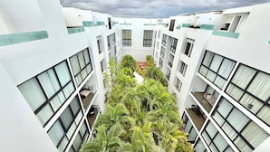 A multi-story building with a central atrium lined with plants, large windows, and balconies. - Central 2 BR PH Gym, Private Rooftop, Garage, 406 (Playa del Carmen - Centro)