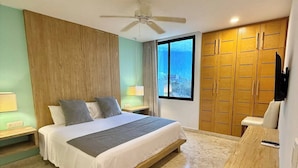 A bedroom with a bed, wooden wardrobe, a desk, a ceiling fan, and a window with a view. - Central 2 BR PH Gym, Private Rooftop, Garage, 406 (Playa del Carmen - Centro)