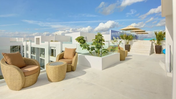 A rooftop terrace with wicker furniture, potted plants, and a glass balustrade overlooking a cityscape. - Central 2 BR PH Gym, Private Rooftop, Garage, 406 (Playa del Carmen - Centro)