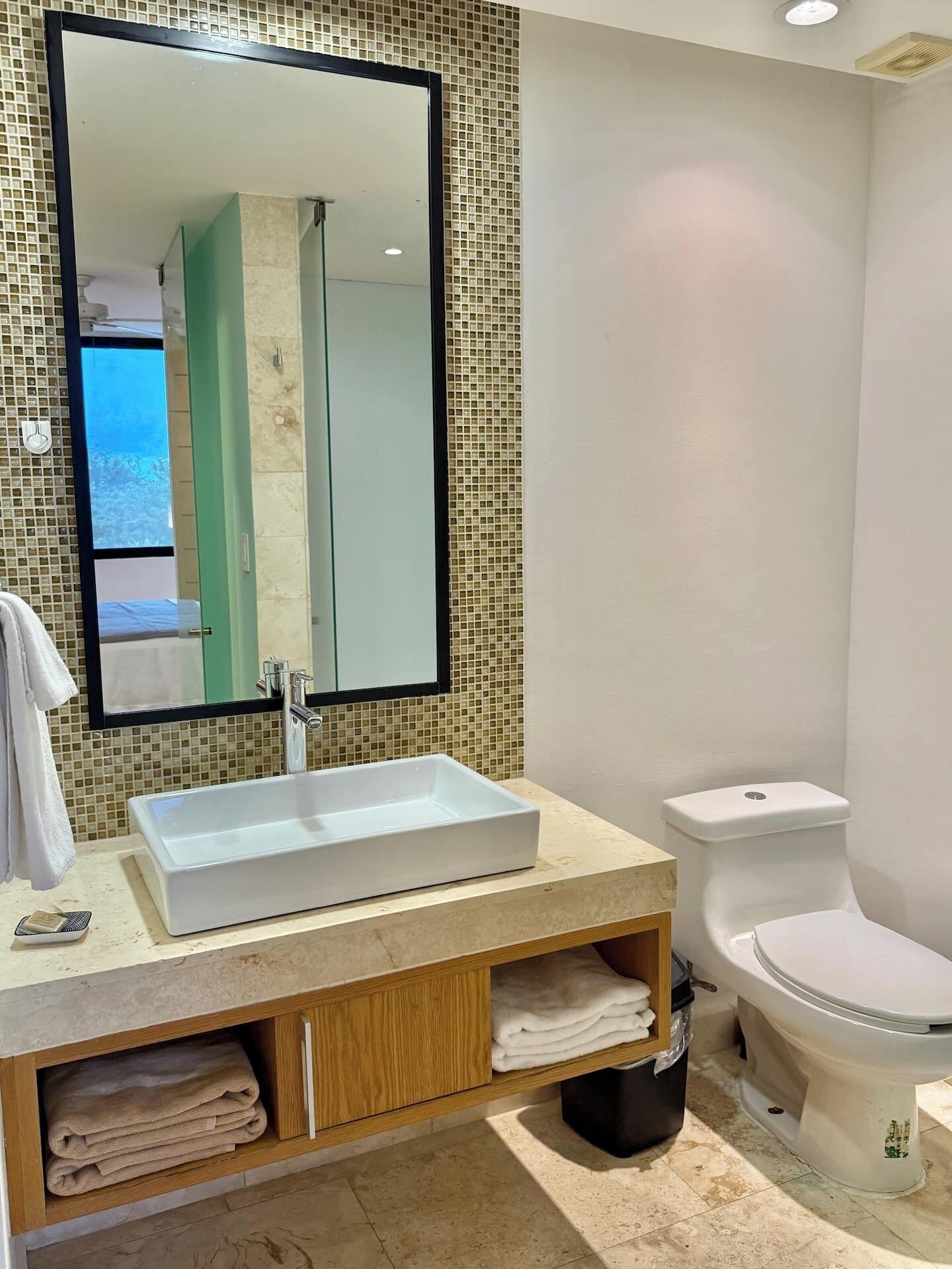 Un baño con un lavabo rectangular, un inodoro y un espejo sobre el lavabo.