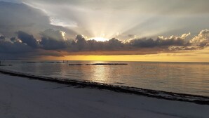 En strand med en vacker solnedgång, ett lugnt hav och en brygga i fjärran.