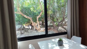Een kamer met een raam, een tafel met een plant, een witte stoel en een houten garderobe met opgevouwen kleding.