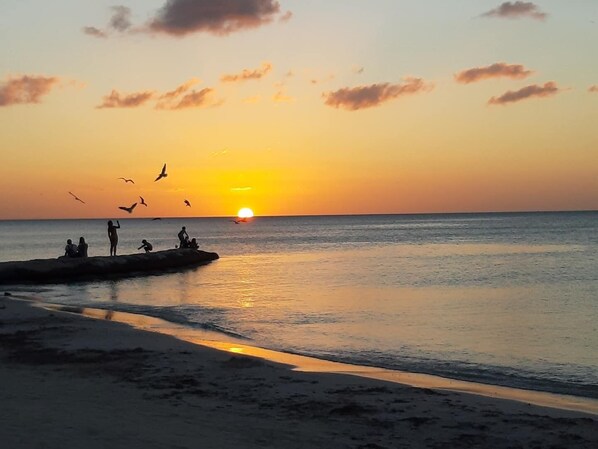 Ein Sonnenuntergang über einem ruhigen Meer mit Silhouetten von Personen auf einem Steg.