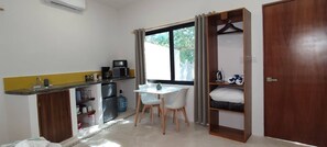 Ein kleines Zimmer mit einer Küchenzeile, einem Esstisch, einem Kleiderschrank und einem Fenster.