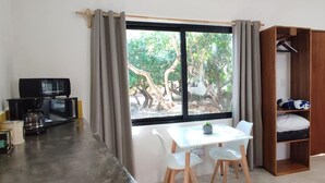 Habitació amb taula de dinar, cadires, televisió, màquina de cafè, armari de fusta i finestra amb vista a arbres.