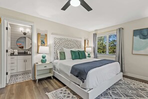 A bedroom with a bed, bedside tables, a nightstand, a window with curtains, and a view of greenery outside. - New Cabin | Fam-Friendly | AC | Game Room | Hottub (Flagstaff)