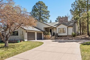 A two-story house with a stone chimney, a garage, and a driveway leading to the front door. - New Cabin | Fam-Friendly | AC | Game Room | Hottub (Flagstaff)