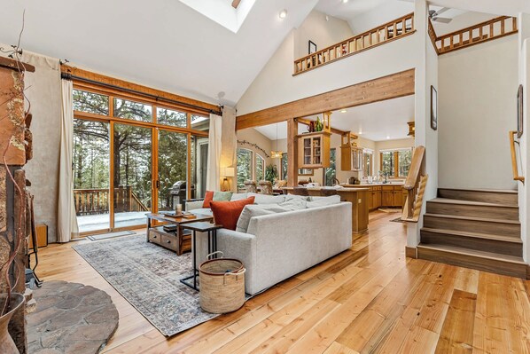 A spacious living area with a large sofa, a dining table, and a kitchen in the background. - NEW 4BR | Cabin & Pines Hideaway | AC | Craftsman (Flagstaff)