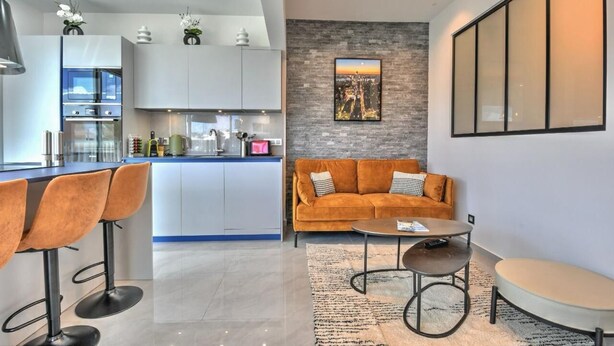 A modern kitchen with white cabinets, a bar area with stools, a gray stone accent wall, and a large framed cityscape picture. - Apartment TalyJay - 2 bedrooms with swimming pools (Nettle Bay)