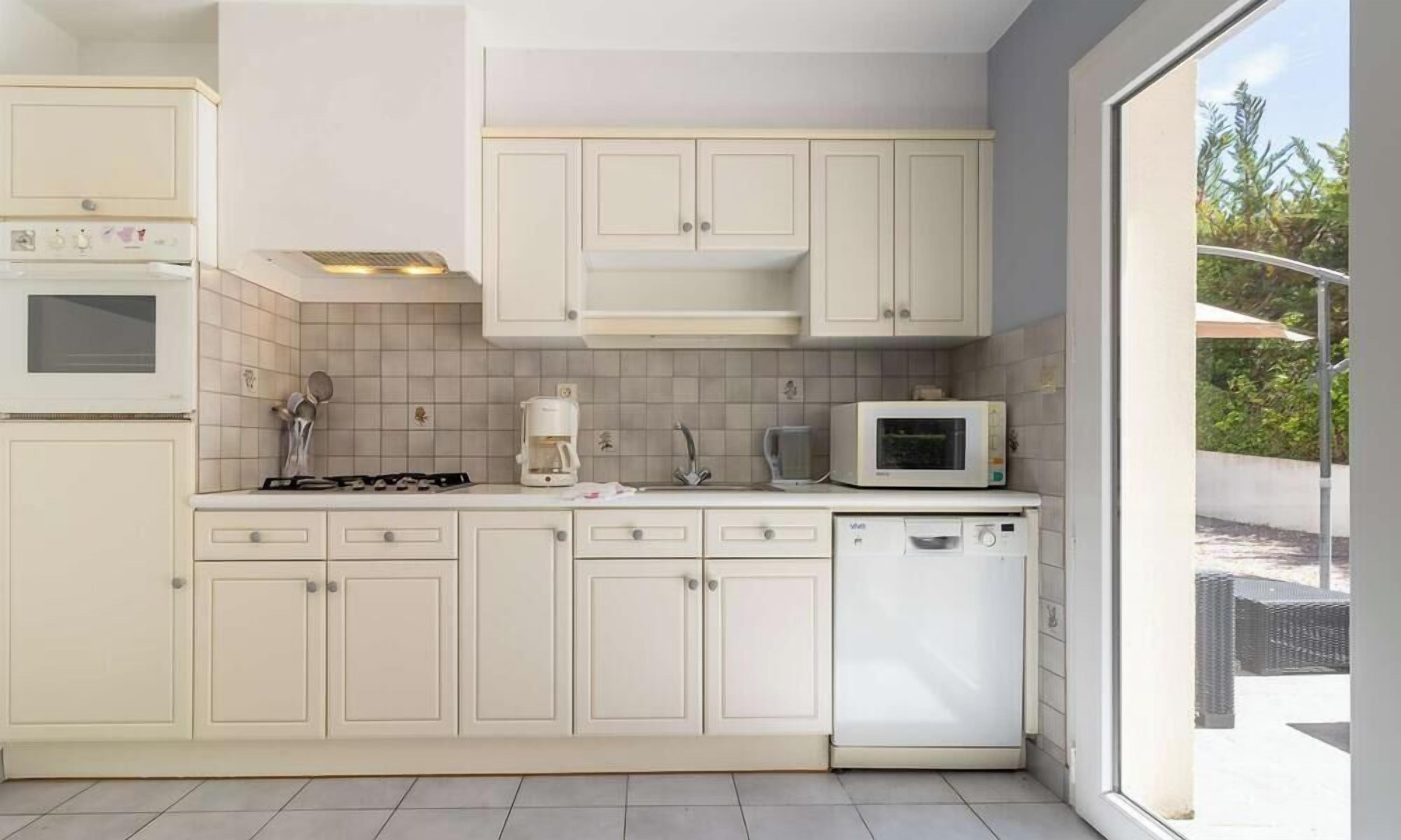 Een moderne keuken met witte kastjes, een magnetron, een koffiezetapparaat en een vaatwasser.