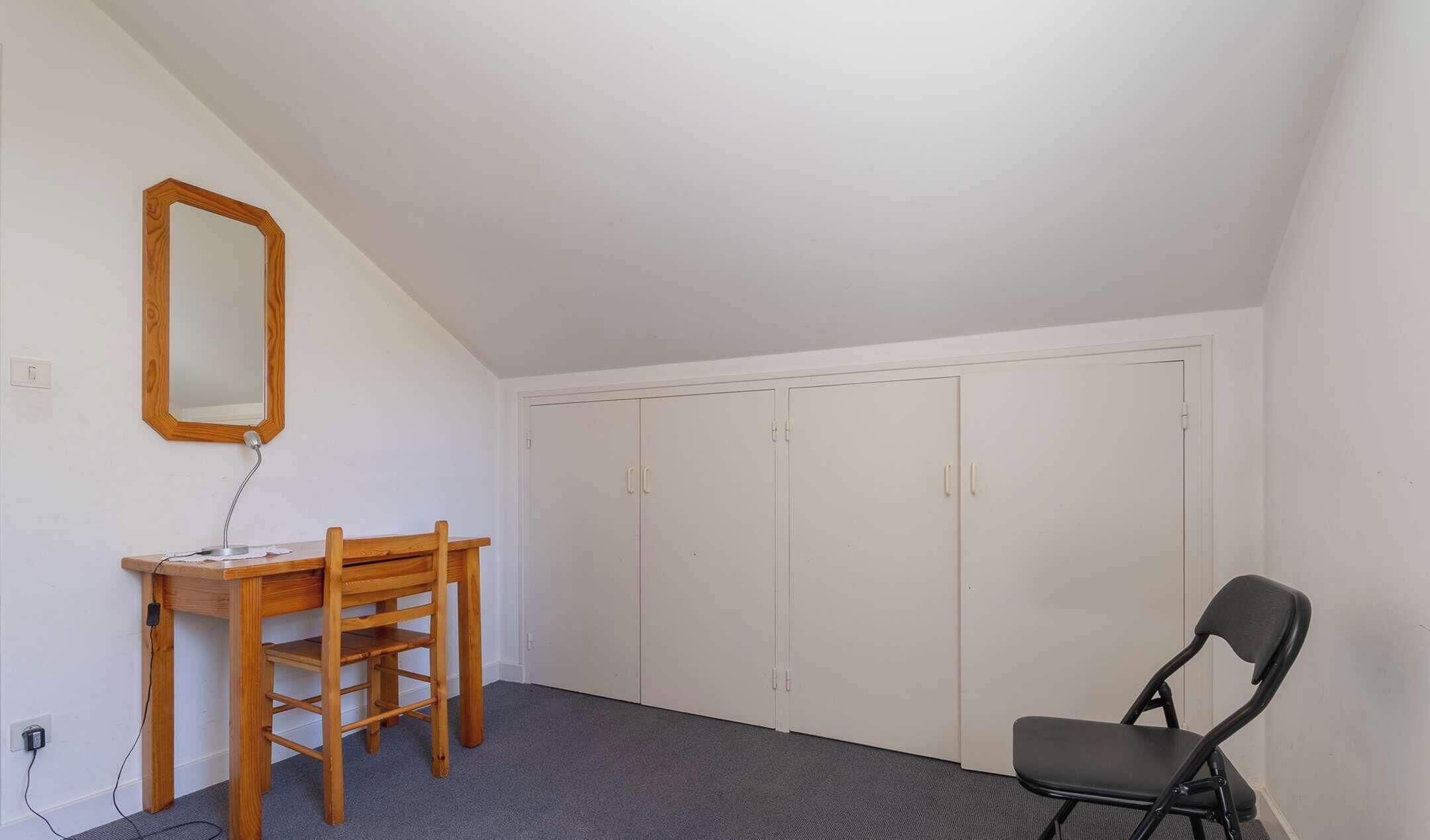 A room with a desk, chair, wardrobe, and a mirror.