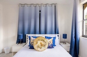 Ein Schlafzimmer mit einem Bett, zwei Nachttischen, einer Lampe auf jedem Tisch und einem Fenster mit Vorhängen.
