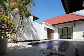 A swimming pool with a red roof, white walls, and a potted plant with pink flowers. -  Blue Marlin Villas Legian (Legian)