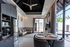A modern kitchen with a dining area, a ceiling fan, and a large window with a view. -  Blue Marlin Villas Legian (Legian)
