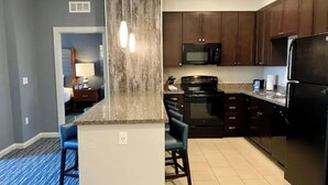 A modern kitchen with dark wooden cabinets, a black refrigerator, and a microwave. There is a blue carpeted area with two bar stools. - Club Wyndham Park City--2BR Deluxe-- Fireplace - (Park City)