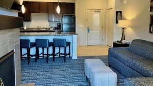 A modern kitchen with dark cabinets, a central island with bar stools, a dining area with a sofa and ottoman, and a hallway leading to a door. - Club Wyndham Park City--2BR Deluxe-- Fireplace - (Park City)