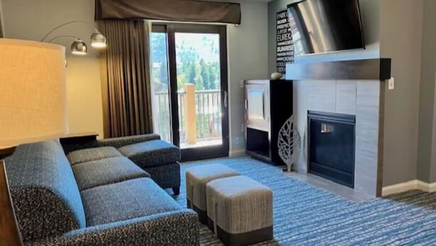 A living room with a sofa, ottoman, fireplace, flat-screen TV, and a view of the outdoors. - Club Wyndham Park City--2BR Deluxe-- Fireplace - (Park City)