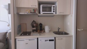 A compact kitchenette with a microwave, a coffee maker, a sink, and a dishwasher. - Charmant T2 vue mer pour deux avec piscine (ARZON)