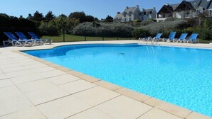 A swimming pool with lounge chairs and a paved deck. - Charmant T2 vue mer pour deux avec piscine (ARZON)