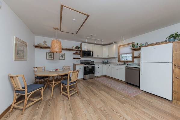 A modern kitchen with white cabinets, a dining table with chairs, a microwave, a refrigerator, and a wooden floor.