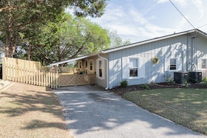 A single-story house with a covered porch, a wooden fence, and a paved driveway.
