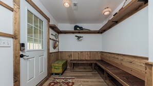 Een kamer met een houten bankje, een kamerbreed tapijt, een koffer en een gitaar op een plank.