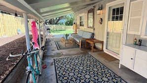 Een overdekt terras met een fiets, een decoratief vloerkleed en tuinmeubilair.