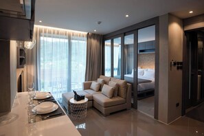 A modern hotel room with a sofa, a dining area with a table set for two, and a bed with a view. - Modern 1-bedroom Suite With Pool Access in Kamala, Phuket (Kamala)
