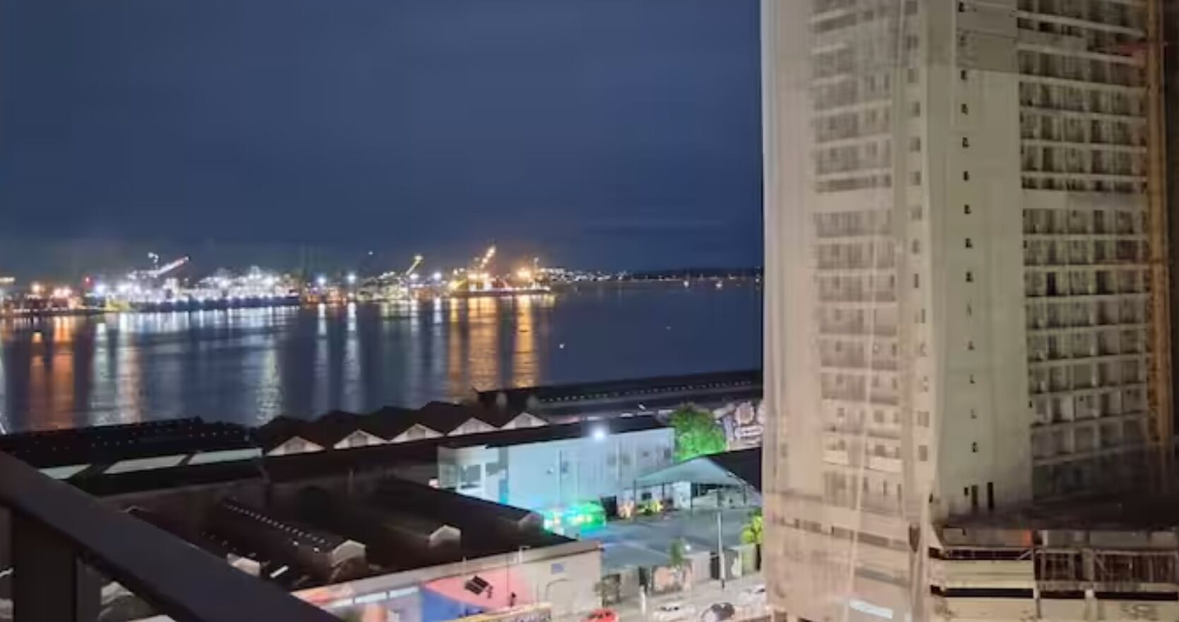 Ein Nachtblick auf ein Ufergebiet mit Gebäuden, einer Brücke und einem Wasserspiegel.