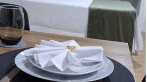 Ett välordnat matbord med en vikt servett, ett kristallglas med rött vin och en tallrik placerad på en underlägg.