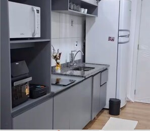 A modern kitchen with grey cabinets, a white refrigerator, a microwave, and a sink. - Studio with Sea View | Ocean View Studio with Pool, WiFi & AC (Rio de Janeiro)