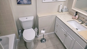 Une salle de bain équipée de toilettes, d’un lavabo et ornée d’un tableau représentant un paysage de canal.