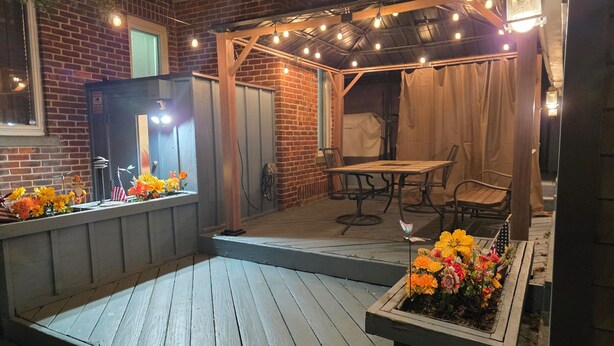 Un espace patio avec une table et des chaises en bois, un arrangement floral et un mur en briques.