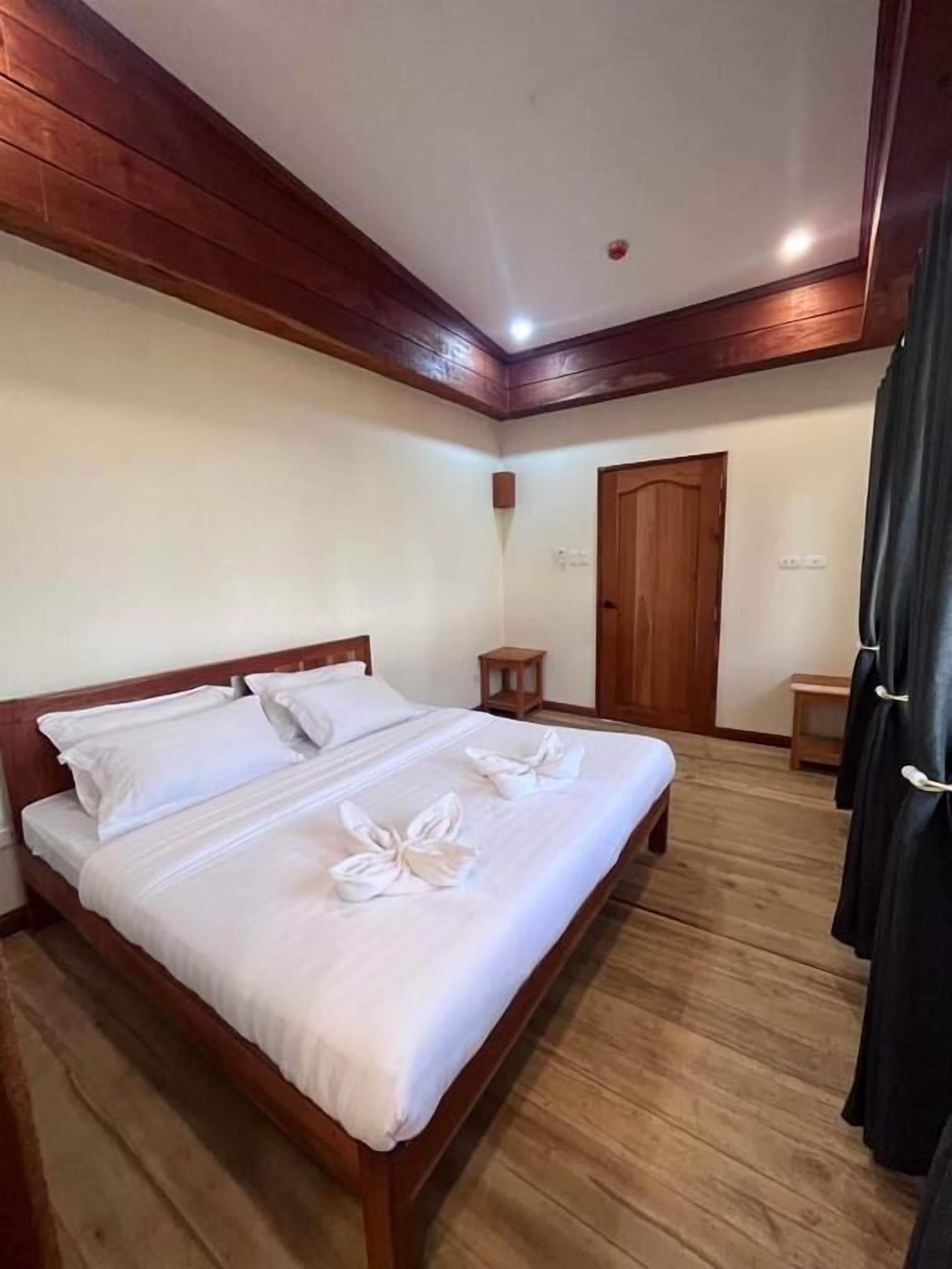 A hotel room with a wooden bed, a bedside table, a nightstand, a door, and a curtain.