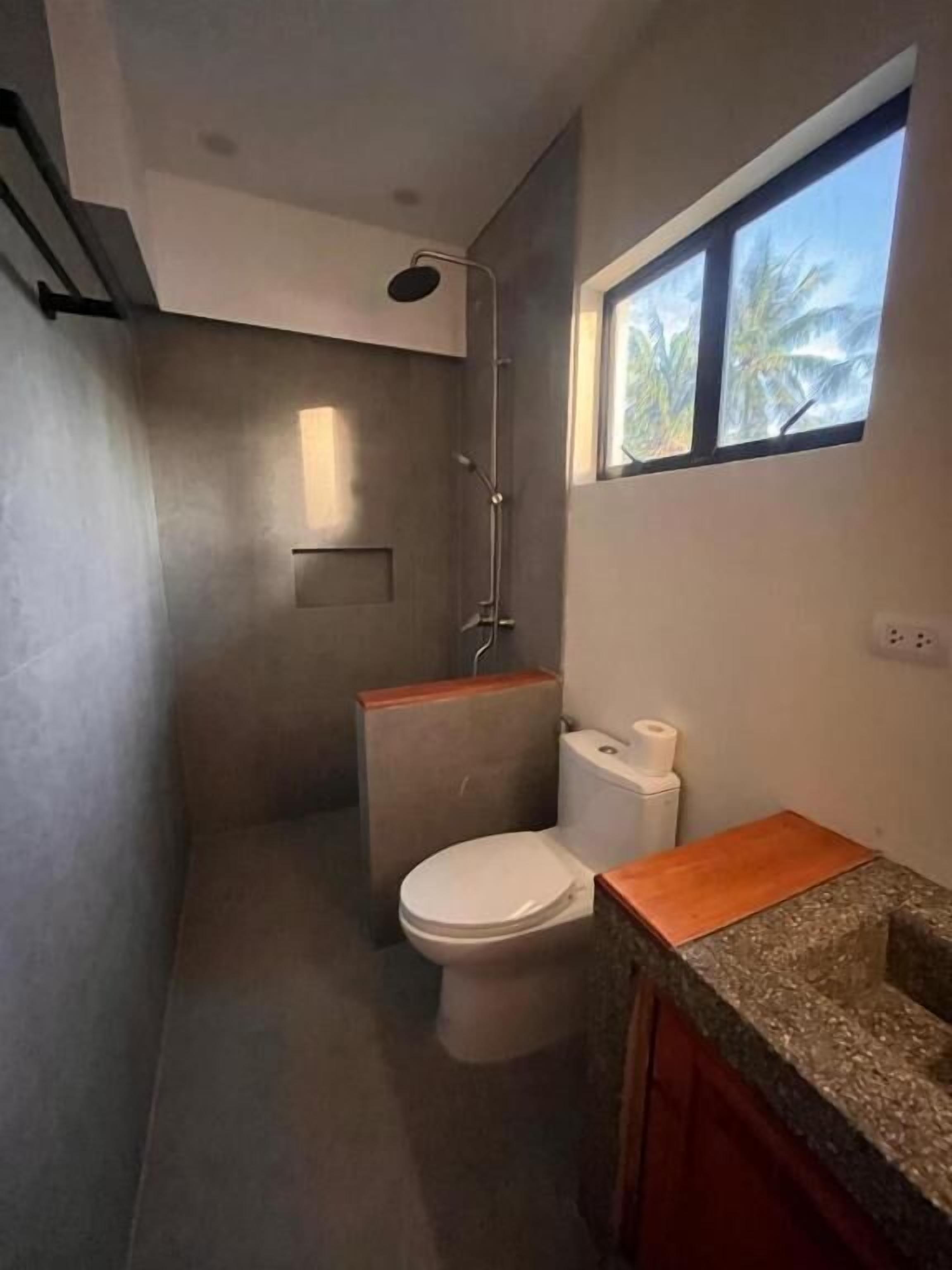 Un baño con ducha, inodoro y ventana.