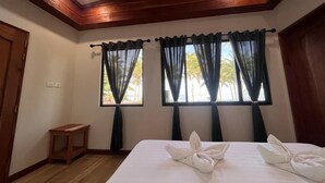 Una habitación de hotel con techo de madera, dos ventanas con cortinas, una cama con toallas y una pequeña mesa de madera.