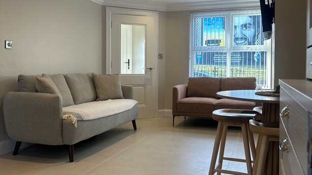 A modern living room with a grey sofa, a brown sofa, a small round table with stools, and a large window with a view. - Derry City Apartment (walking distance to city centre and local amenities) (Londonderry)
