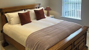 A bedroom with a wooden bed, white bedding, a patterned throw, a nightstand, a lamp, and a window with blinds. - Derry City Apartment (walking distance to city centre and local amenities) (Londonderry)