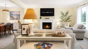 A living room with a fireplace, a sofa, a coffee table, and a television mounted on the wall. - Private Retreat Near Interlochen Arts| Green Lake (Interlochen)