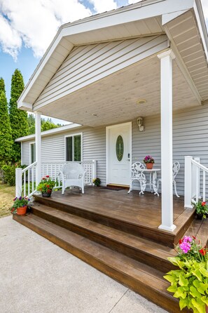 Une maison avec un porche, des balustrades blanches et des marches menant à l’entrée.