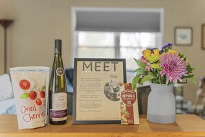 Une table avec une bouteille de vin, un sachet de cerises séchées, un mot encadré, une boîte de chocolats au lait et un vase de fleurs.