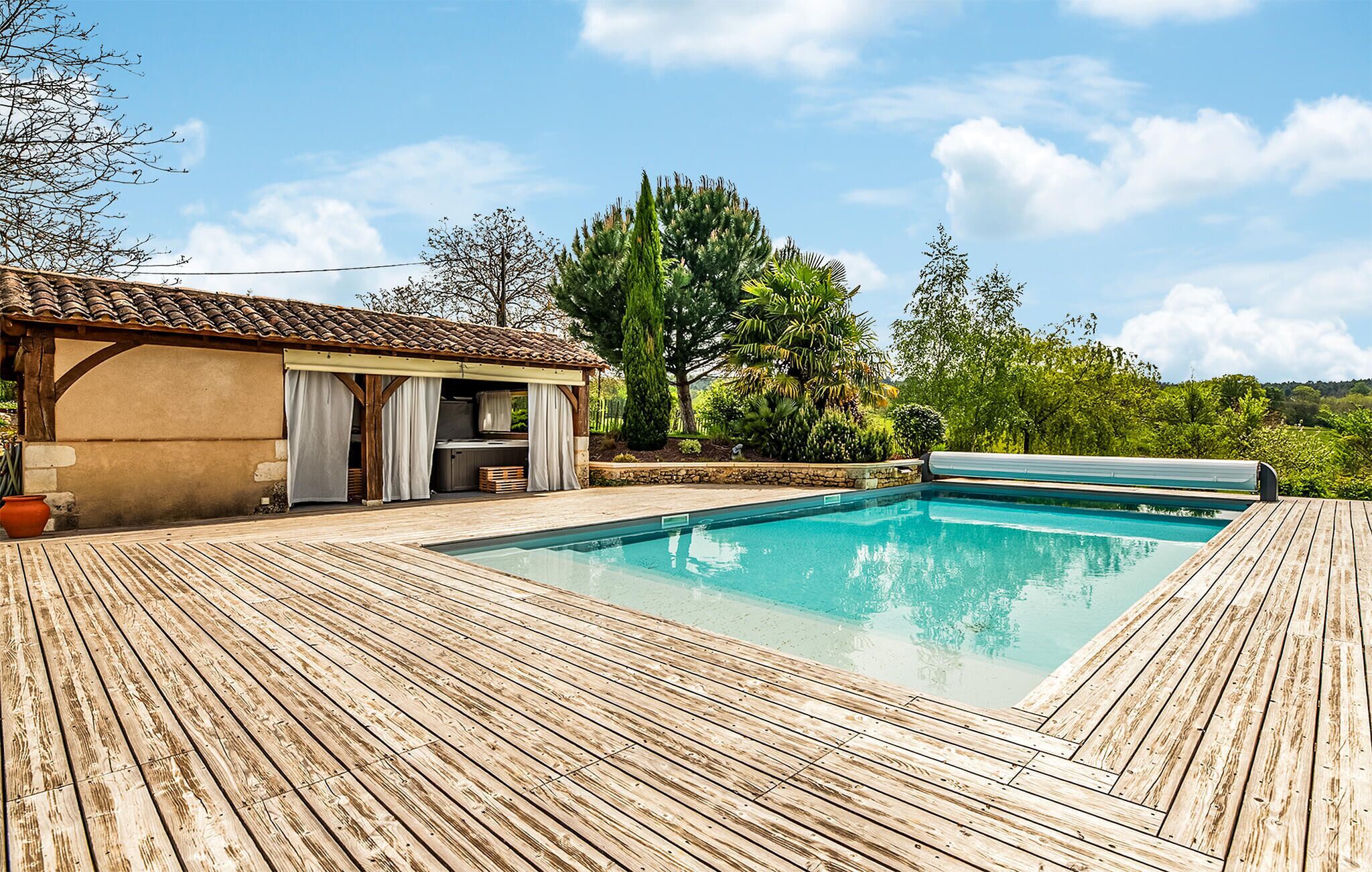 Una terraza de madera rodea una piscina rectangular con un pérgola y zona de estar al aire libre.