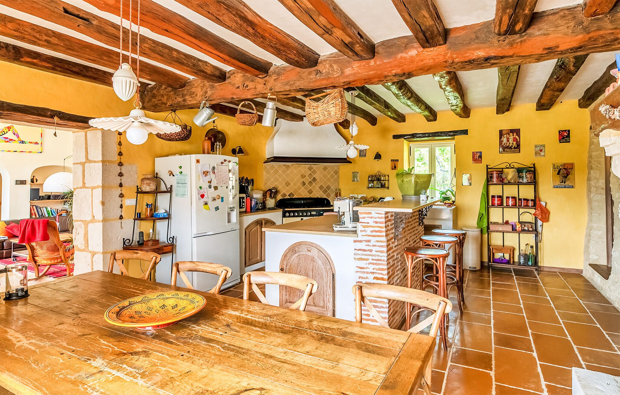 A rustic kitchen with exposed wooden beams, a central island with stools, and a dining table with chairs.